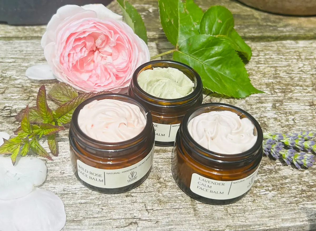 Open jars of Wild Rose, Serene Green and Lavender Calm face balms on weathered wood with a pink rose, mint and lavender